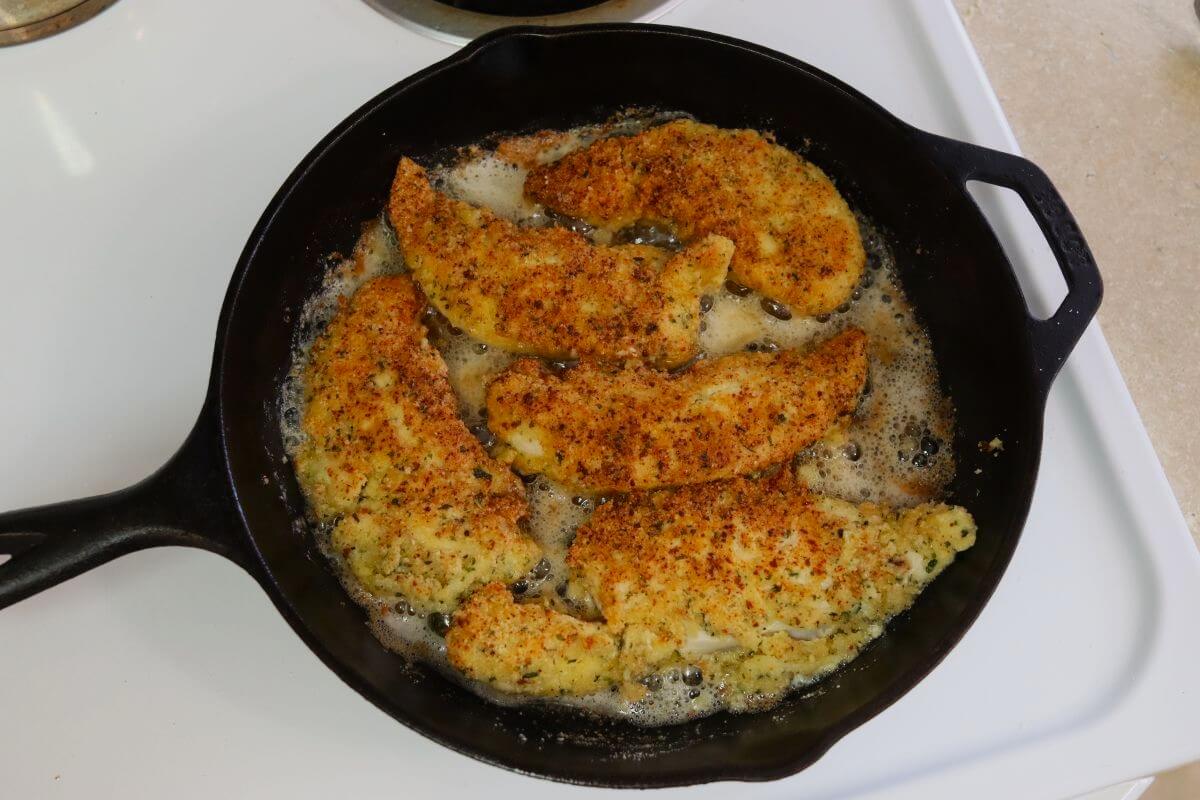 Almond crusted chicken tenders frying in oil in a cast iron skillet.