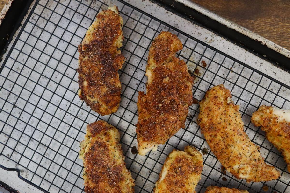 Almond crusted chicken tenders cooling on a wire rack over baking sheet.