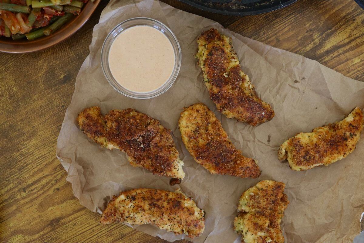 Six almond crusted chicken tenders on parchment paper with dipping sauce.