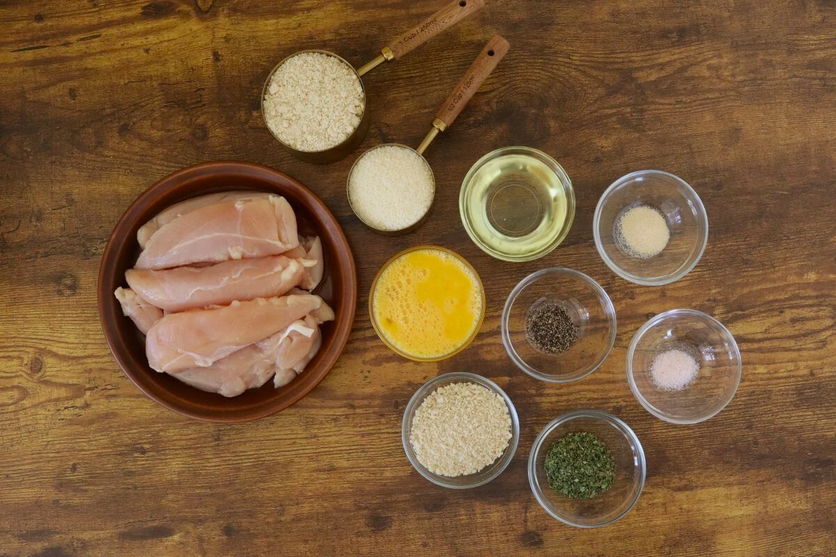 Raw chicken tenders with almond flour, breadcrumbs, egg wash, oil, and seasonings.