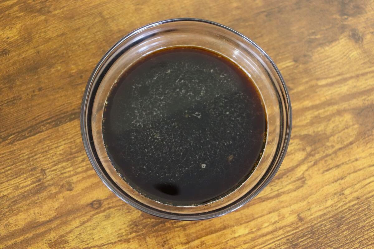 Glass bowl filled with dark marinade on wooden surface.