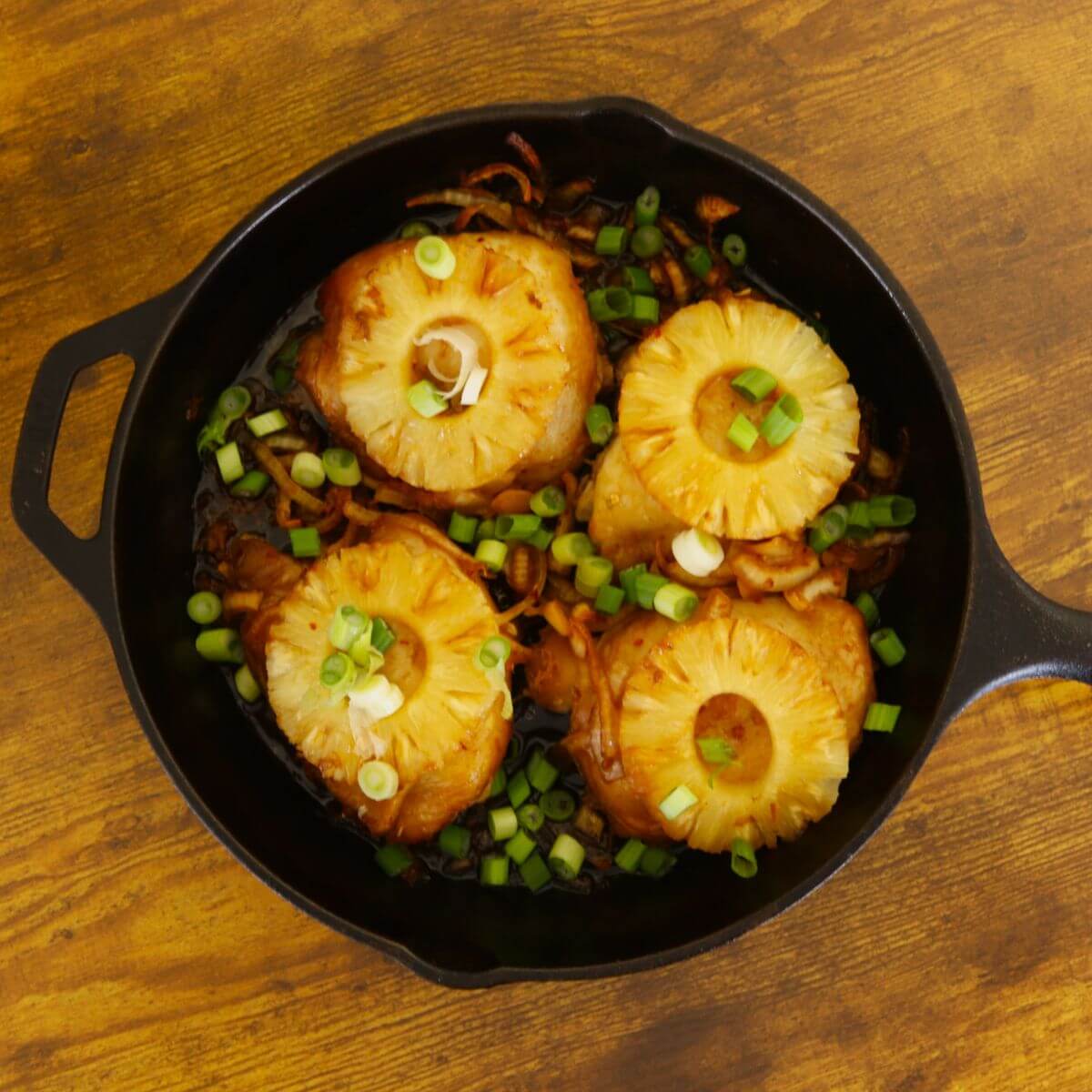 Chicken thighs with pineapple rings and scallions in cast iron pan.