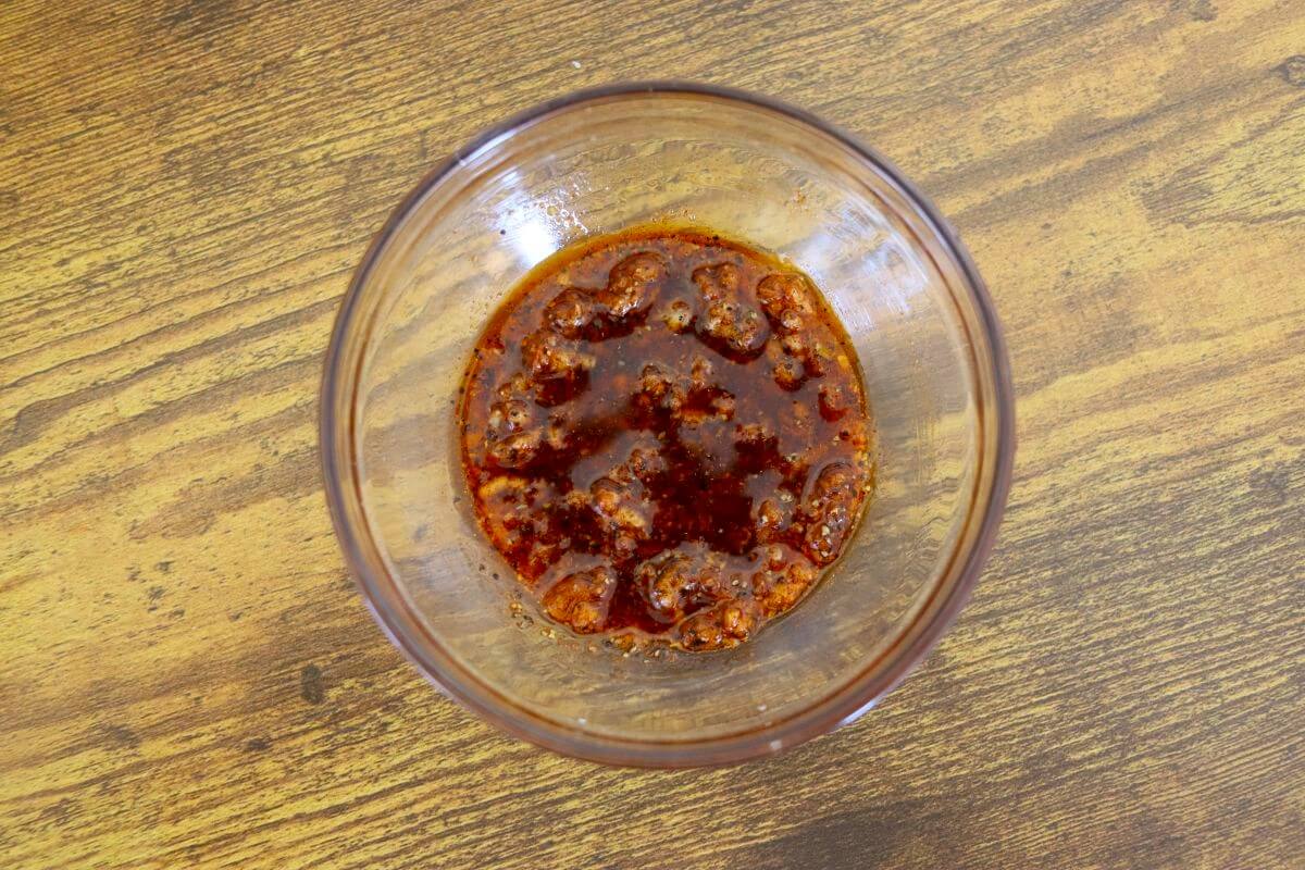 Seasoning mixture with olive oil, garlic, smoked paprika, salt, and pepper combined in a glass bowl.