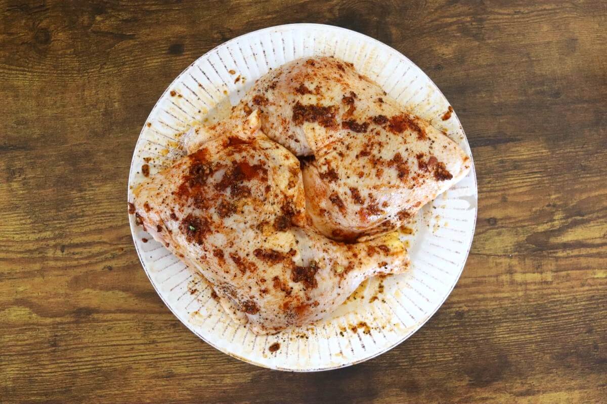 Seasoned chicken leg quarters resting on a plate before baking.