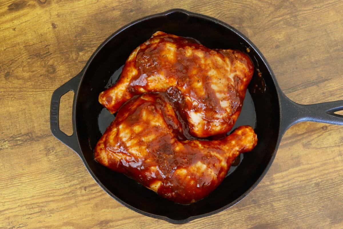 BBQ sauce–coated chicken leg quarters arranged in a cast iron skillet before baking.