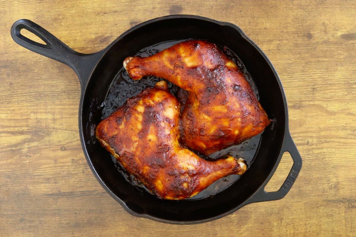 Oven-baked BBQ chicken leg quarters with caramelized sauce in a cast iron skillet.
