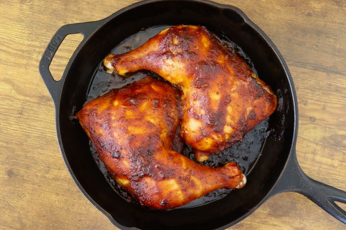 BBQ chicken leg quarters baked in a cast iron skillet with a caramelized barbecue sauce finish.