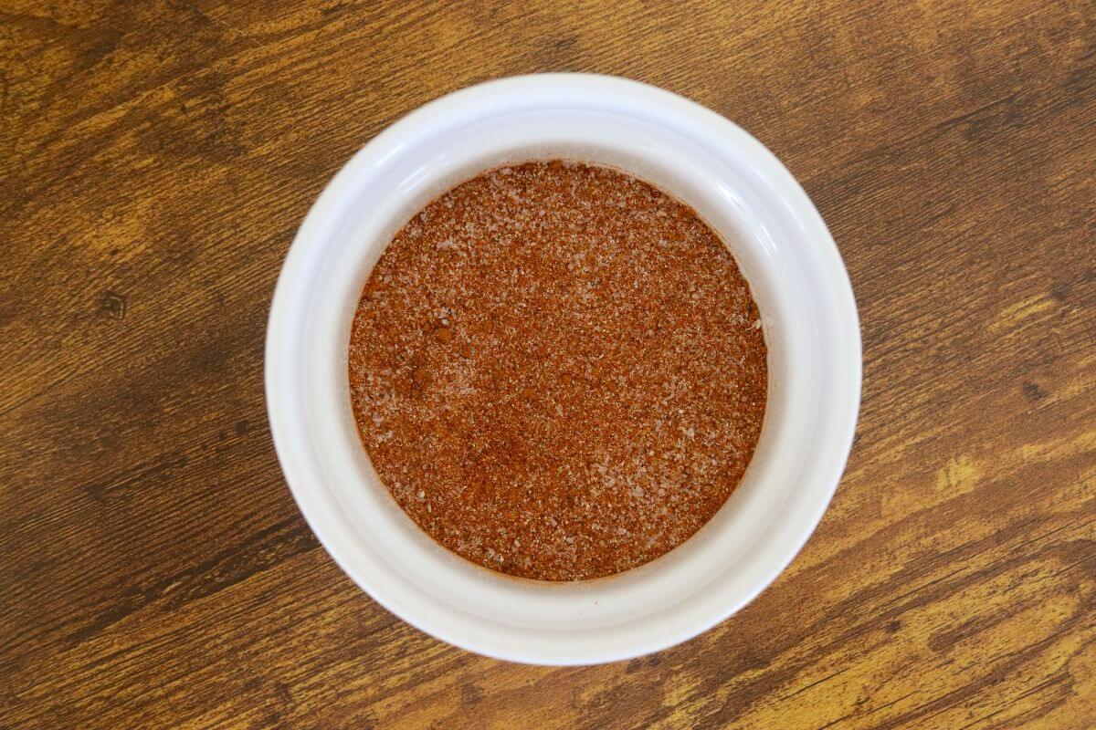 Mixed ground spices in a small white bowl on a wooden surface.