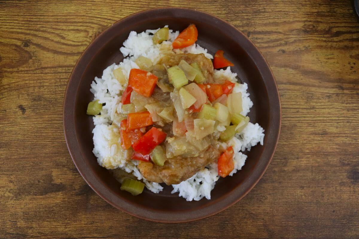 Chicken with onions, bell peppers, and celery served over white rice on a brown plate.