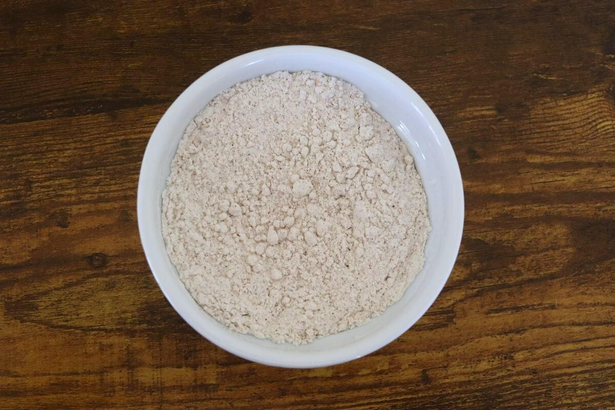 Seasoned flour mixture in a white bowl on a wooden surface.