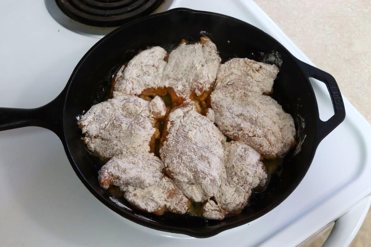 Flour-coated chicken thighs arranged in a cast iron skillet.