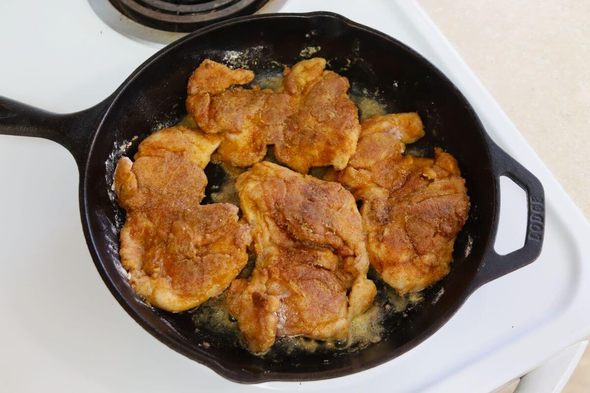 Chicken thighs browned in a cast iron skillet with oil.