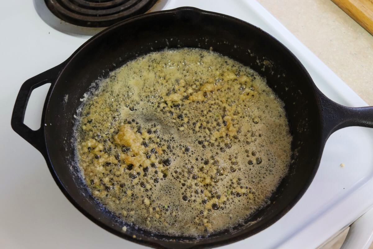 Melted butter and minced garlic bubbling in a cast iron skillet on a stovetop.