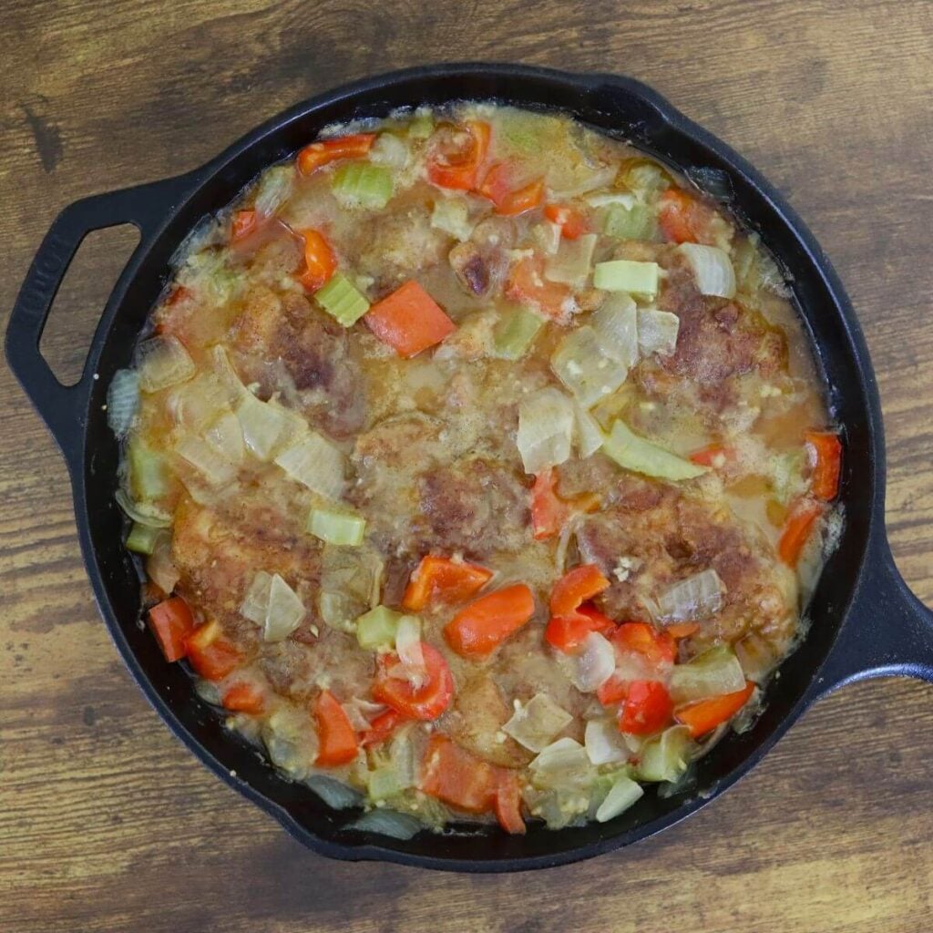 Chicken thighs in a cast iron skillet with onions, bell peppers, and celery in a light broth.