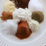 Ground spices and cornstarch arranged in small piles on a white ridged plate with text overlay reading “Homemade Fajita Seasoning Mix – Skip the packet. Mix it in minutes".