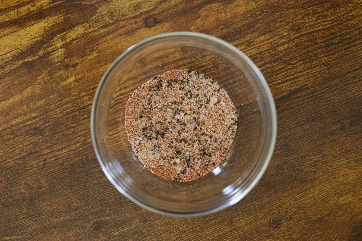 Small glass bowl filled with mixed spices on a wooden surface.