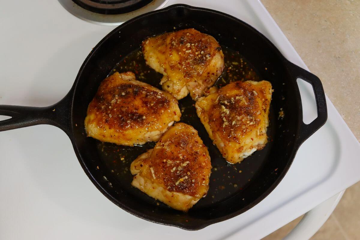 Four chicken thighs coated in sauce in a cast iron skillet on a stovetop.
