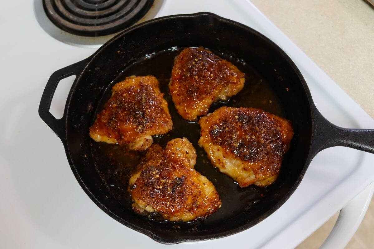Four glazed chicken thighs in a cast iron skillet on a stovetop.