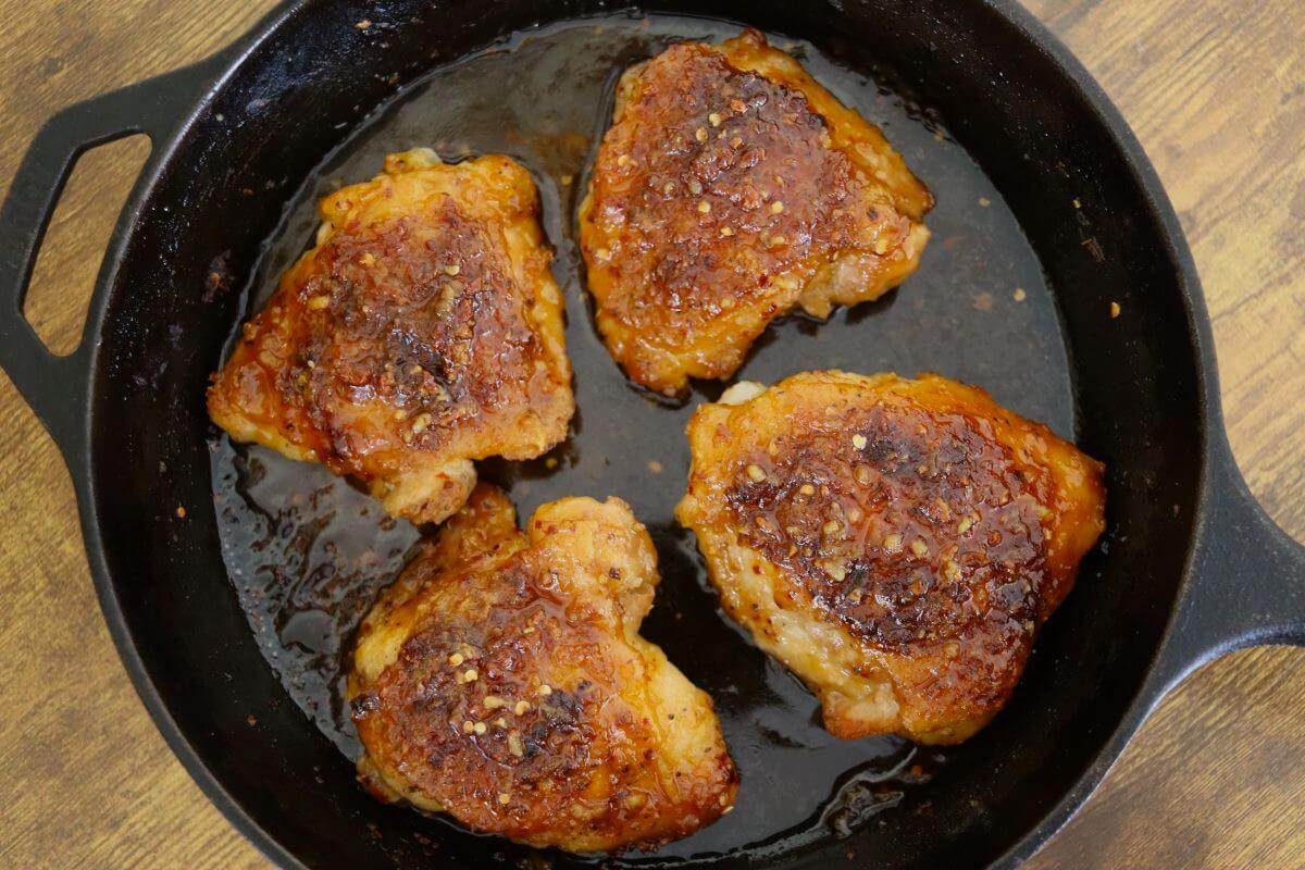 Glazed chicken thighs with red pepper flakes in a cast iron skillet.