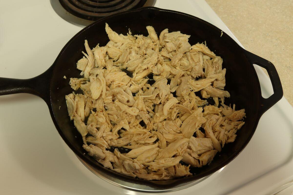 Shredded chicken warming in cast iron skillet on stovetop.