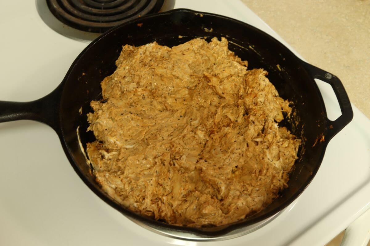 Creamy chicken mixture blended in cast iron skillet on stovetop.