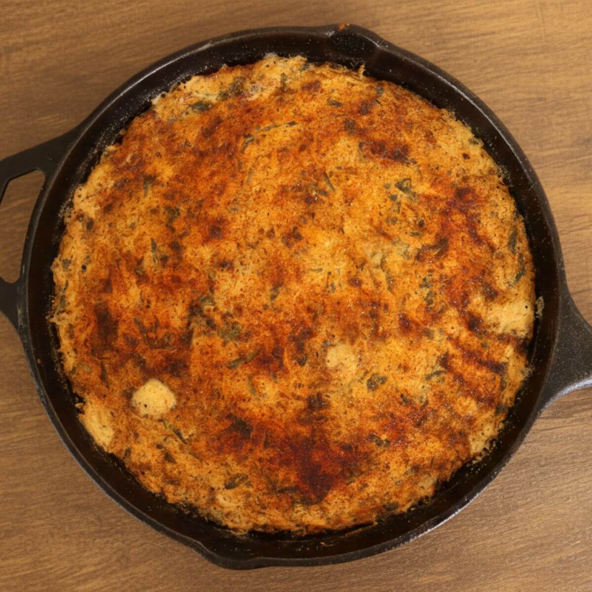 Golden baked chicken dip with herbs in cast iron skillet.