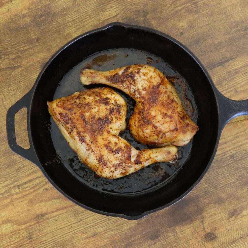 Golden baked, seasoned chicken leg quarters cooked in a cast iron skillet.