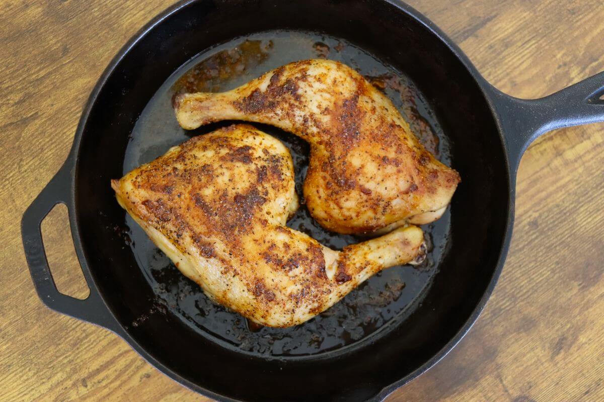 Old-fashioned baked chicken leg quarters with crisp skin in a cast iron skillet.