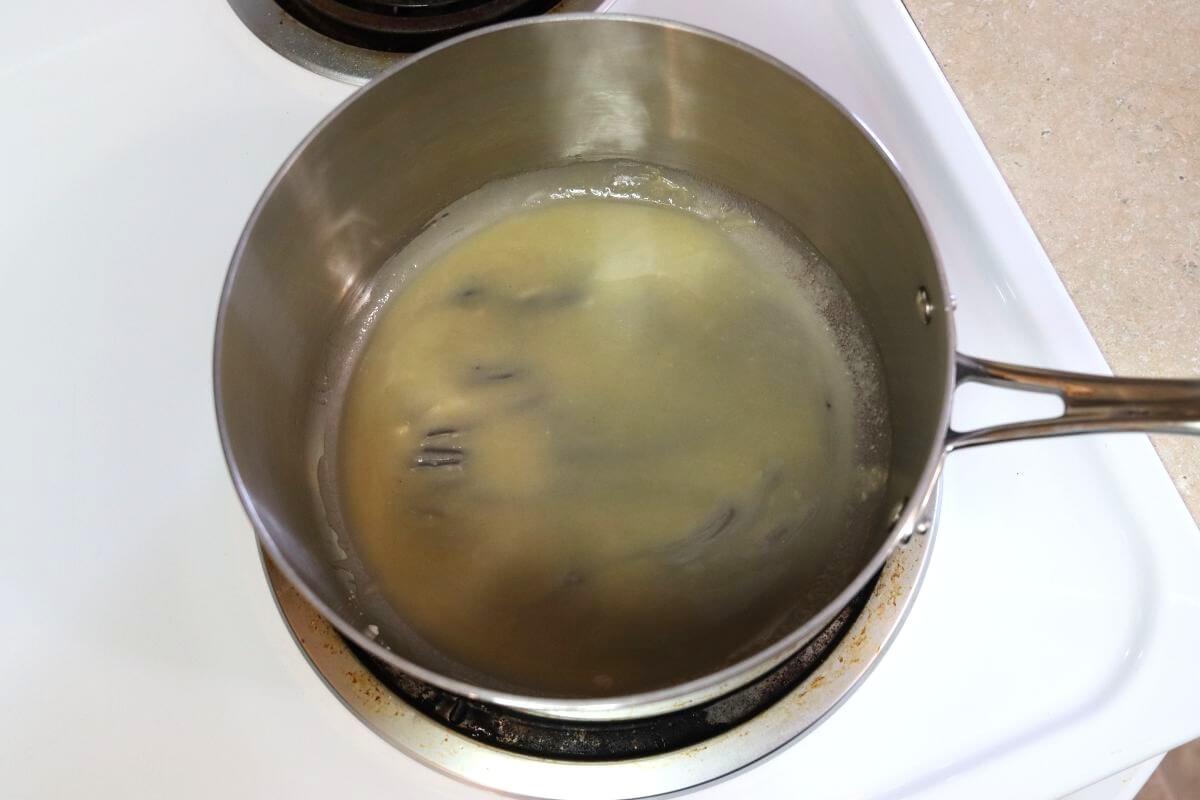 Stainless steel saucepan on a stovetop containing a thin, pale liquid with visible streaks along the bottom.