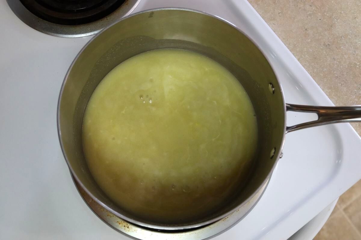 Saucepan on a stovetop filled with a pale, smooth liquid mixture.