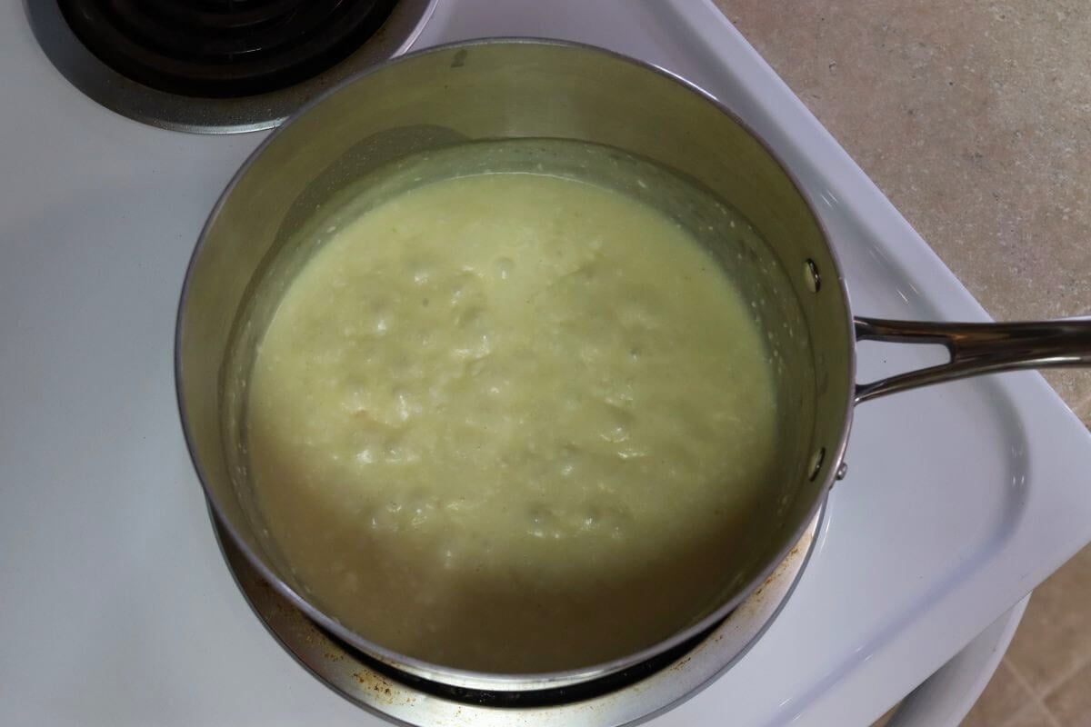 Saucepan on a stovetop filled with a thick, pale mixture with small lumps visible on the surface.