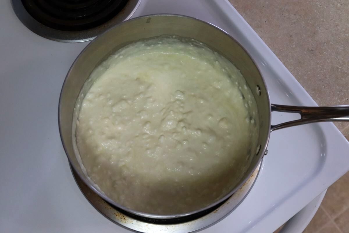 Saucepan on a stovetop filled with a thick, pale mixture showing a bumpy, uneven surface texture.