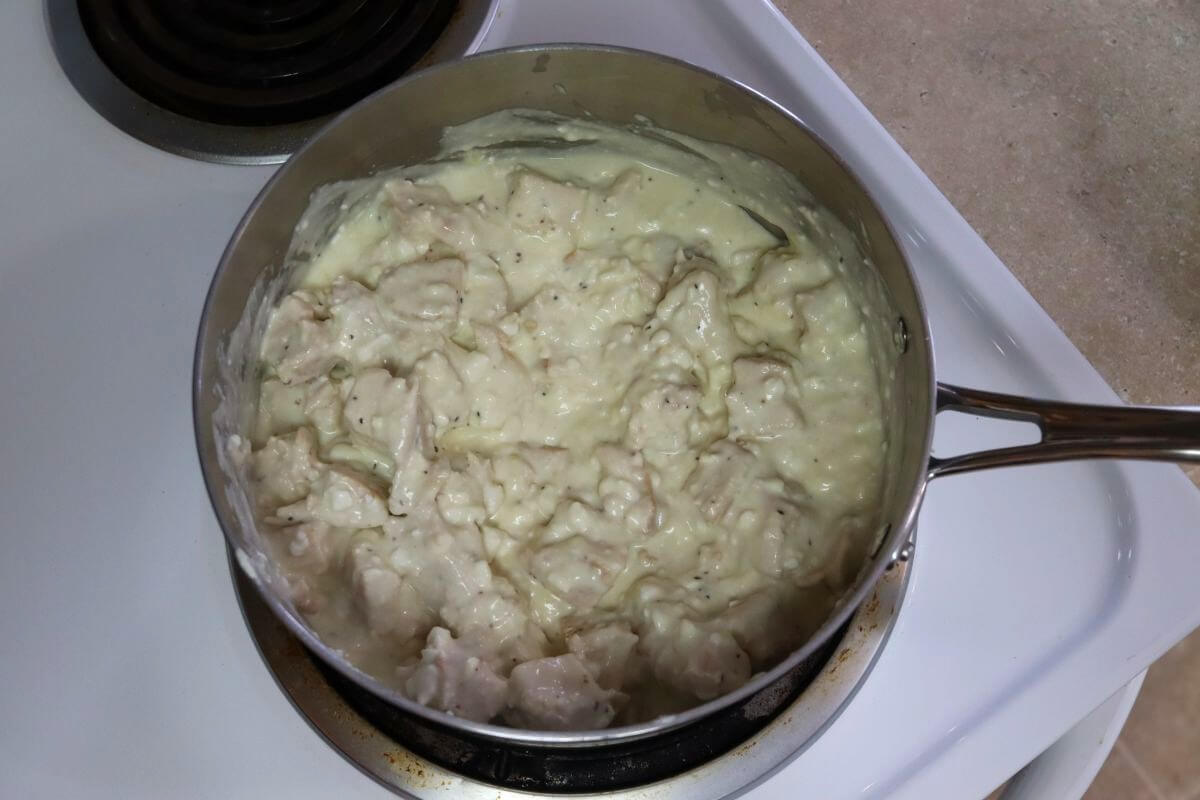 Saucepan on a stovetop filled with a thick, pale mixture containing visible chunks throughout.