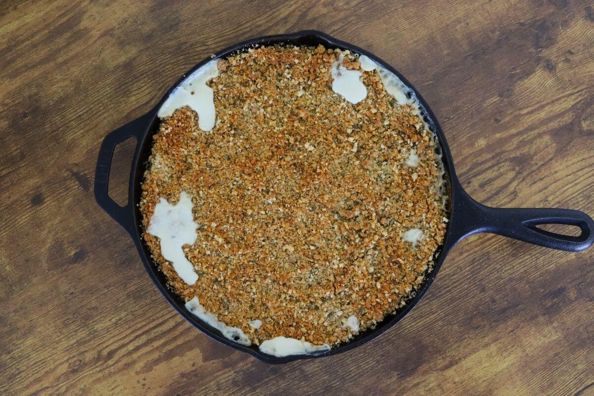 Cast iron skillet filled with browned breadcrumb topping, with small areas of pale sauce visible around the edges.