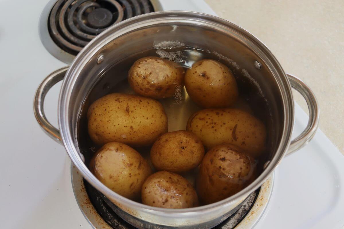 Whole yellow potatoes in water in a stainless steel pot on stovetop.