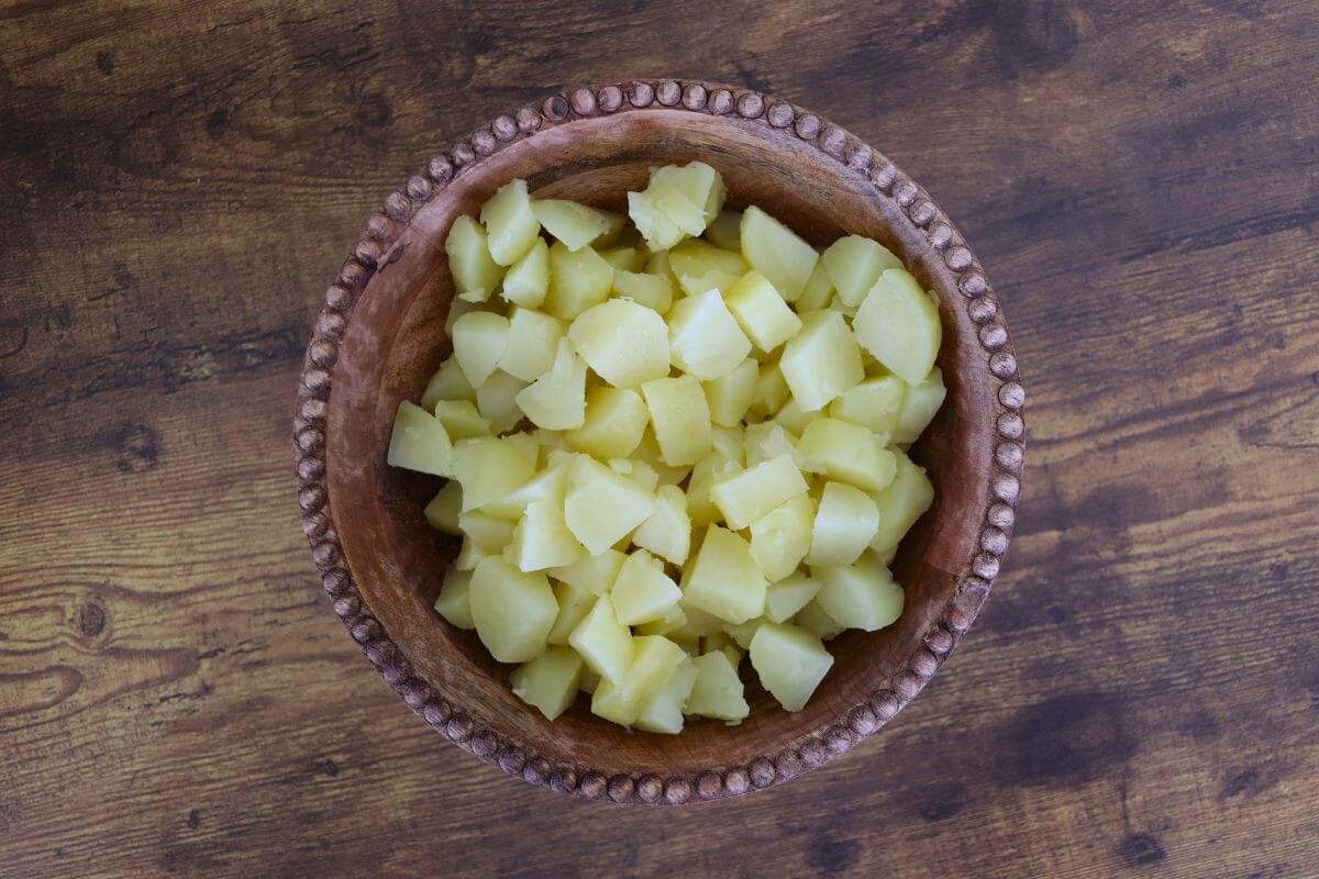 Cubed cooked yellow potatoes in a wooden bowl on a wooden table.
