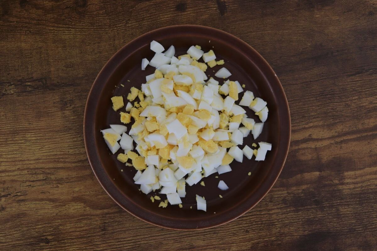 Chopped hard-boiled eggs on a brown plate on a wooden table.