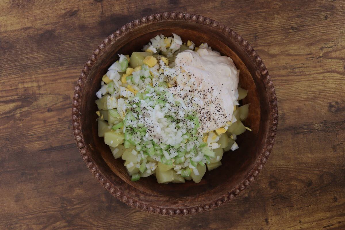 Cubed potatoes, chopped eggs, celery, onion, mayonnaise, salt, and pepper in wooden bowl on table.