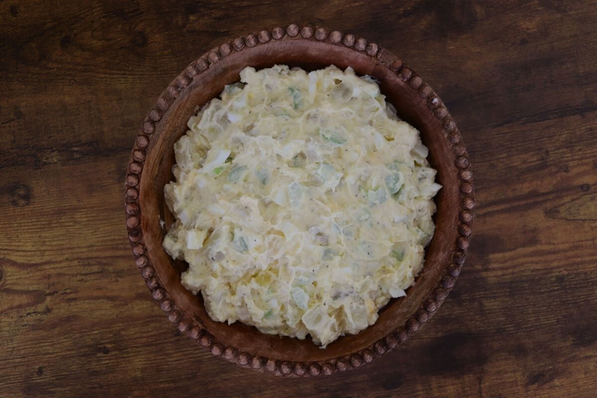 Mixed old-fashioned potato salad in a wooden bowl on a wooden table.