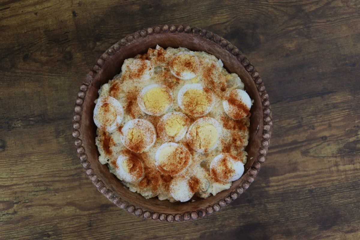 Old-fashioned potato salad garnished with sliced hard-boiled eggs and paprika in a carved wooden bowl.