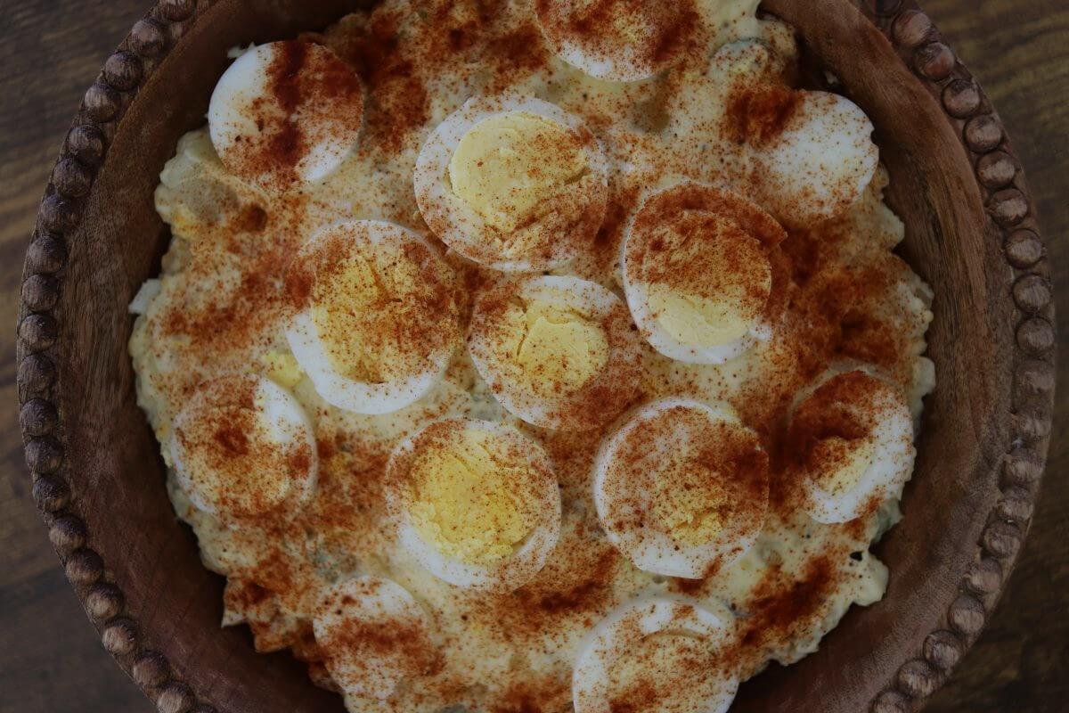 Old-fashioned potato salad topped with sliced eggs and paprika in a wooden bowl.