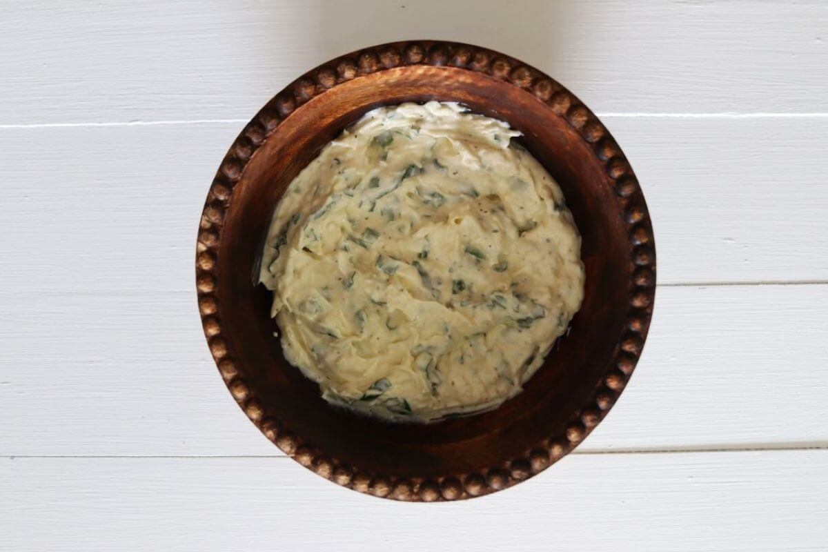 Chicken salad dressing mixture with visible herbs in a brown bowl on a white surface.