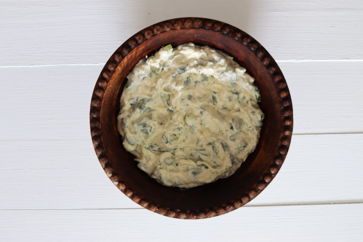 Chicken salad dressing mixture with chopped basil and celery in a round brown bowl on a white tabletop.