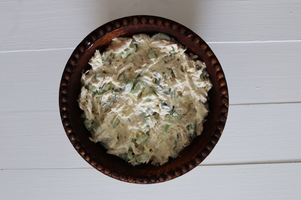 Shredded chicken salad with basil and celery in a brown bowl on a white surface.