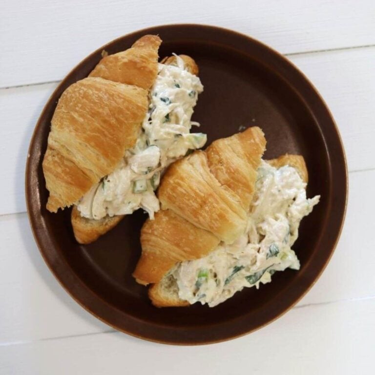 Two basil chicken salad croissant sandwiches filled with shredded chicken on a brown plate.