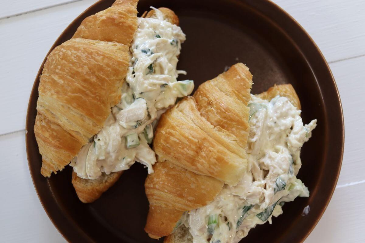 Croissant basil chicken salad sandwiches with visible celery and basil on a brown plate.