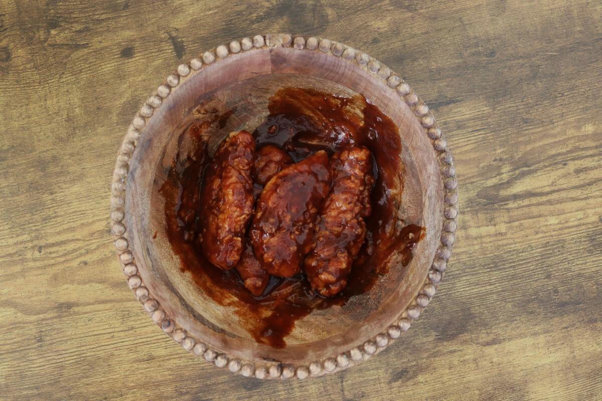 Breaded chicken tenders coated in barbecue sauce in a glass bowl.