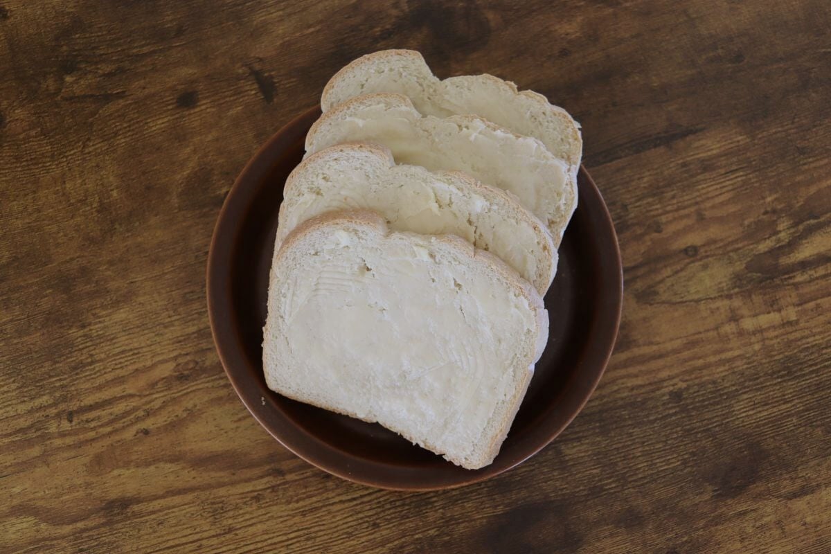 Slices of white bread spread with butter on a brown plate.