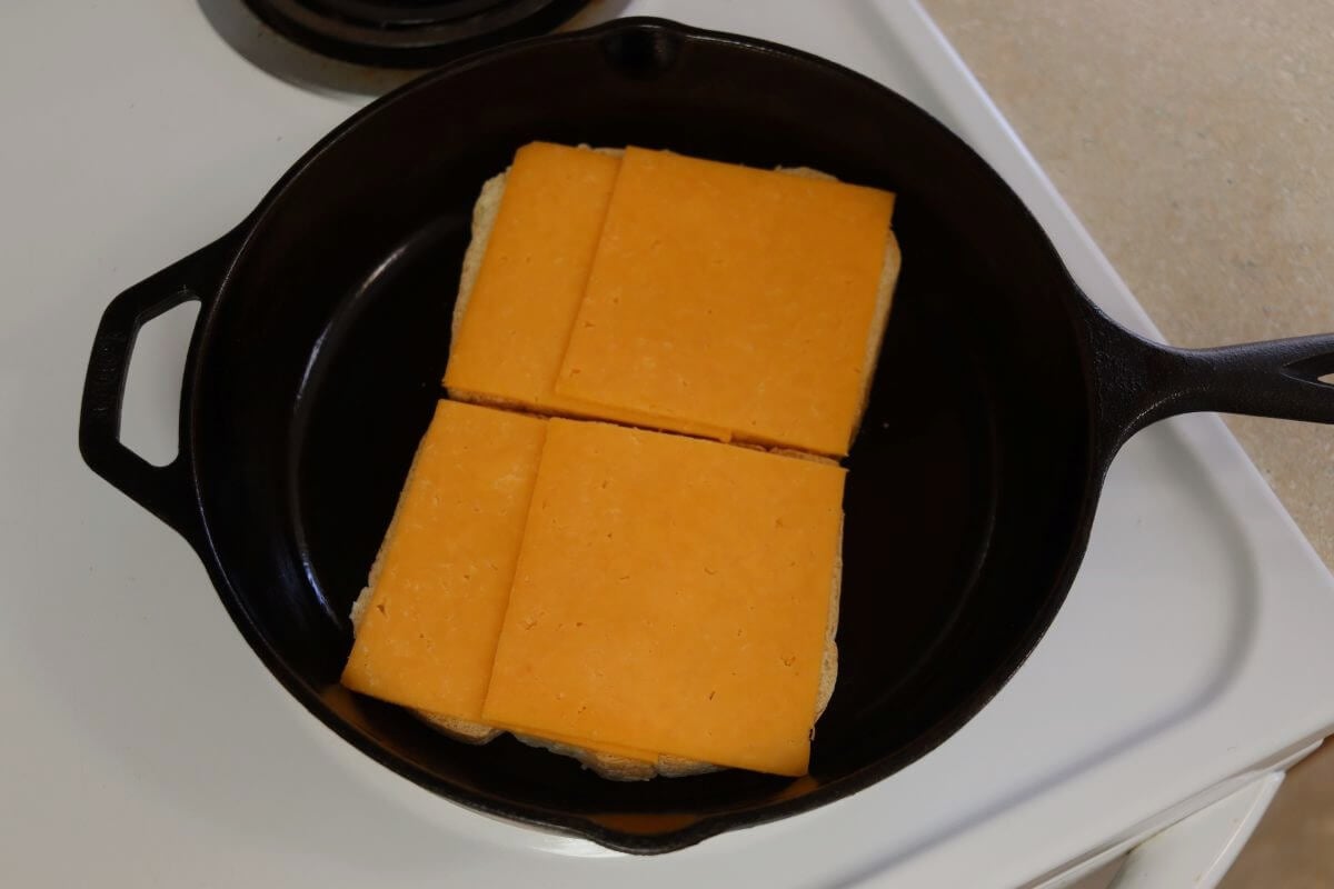 Slices of cheddar cheese placed on bread in a cast iron skillet.