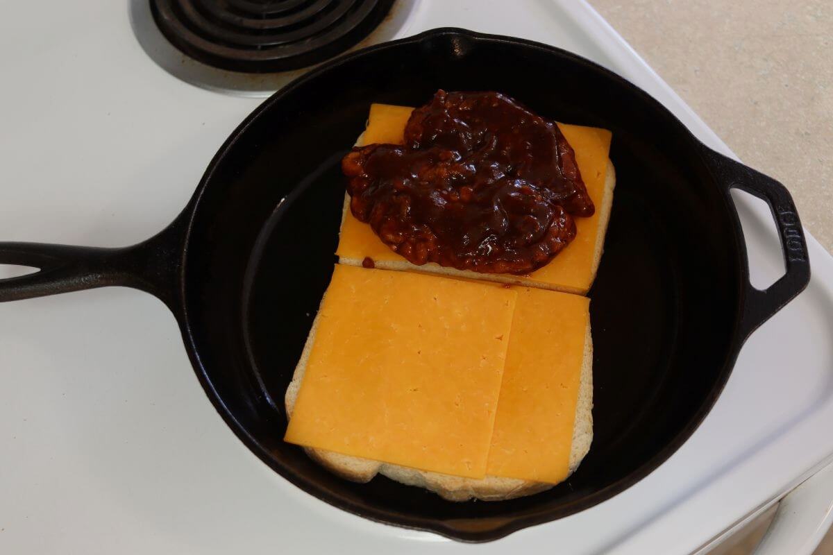 Barbecue chicken placed on cheddar cheese slices in a cast iron skillet.